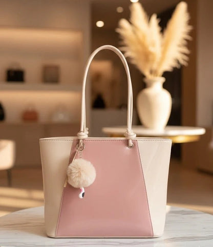 Two-toned handbag with a pom-pom detail on a table in an indoor setting.