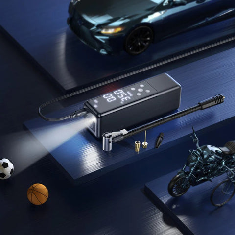 Portable air compressor with accessories on a dark surface, with a car and motorcycle in the background.